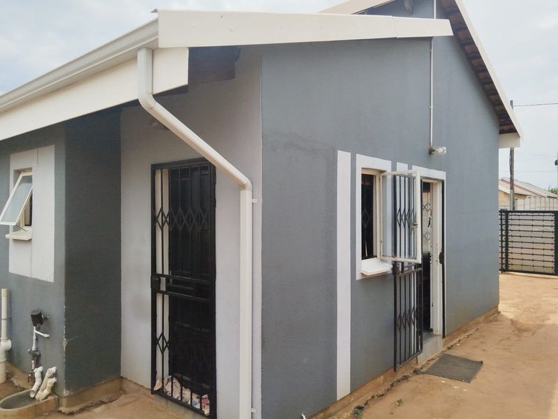 Rear exterior view of the house featuring grey painted walls, white trim, security gates on doors, and functional guttering system.