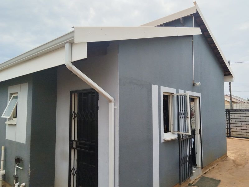 A view of the rear exterior of the house featuring grey painted walls, white trim, guttering, and security gates on the doors and windows.