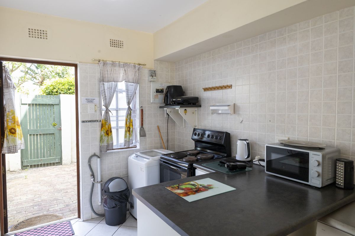 A functional kitchen featuring tiled splashbacks, a freestanding electric stove, and direct access to an outdoor patio area.