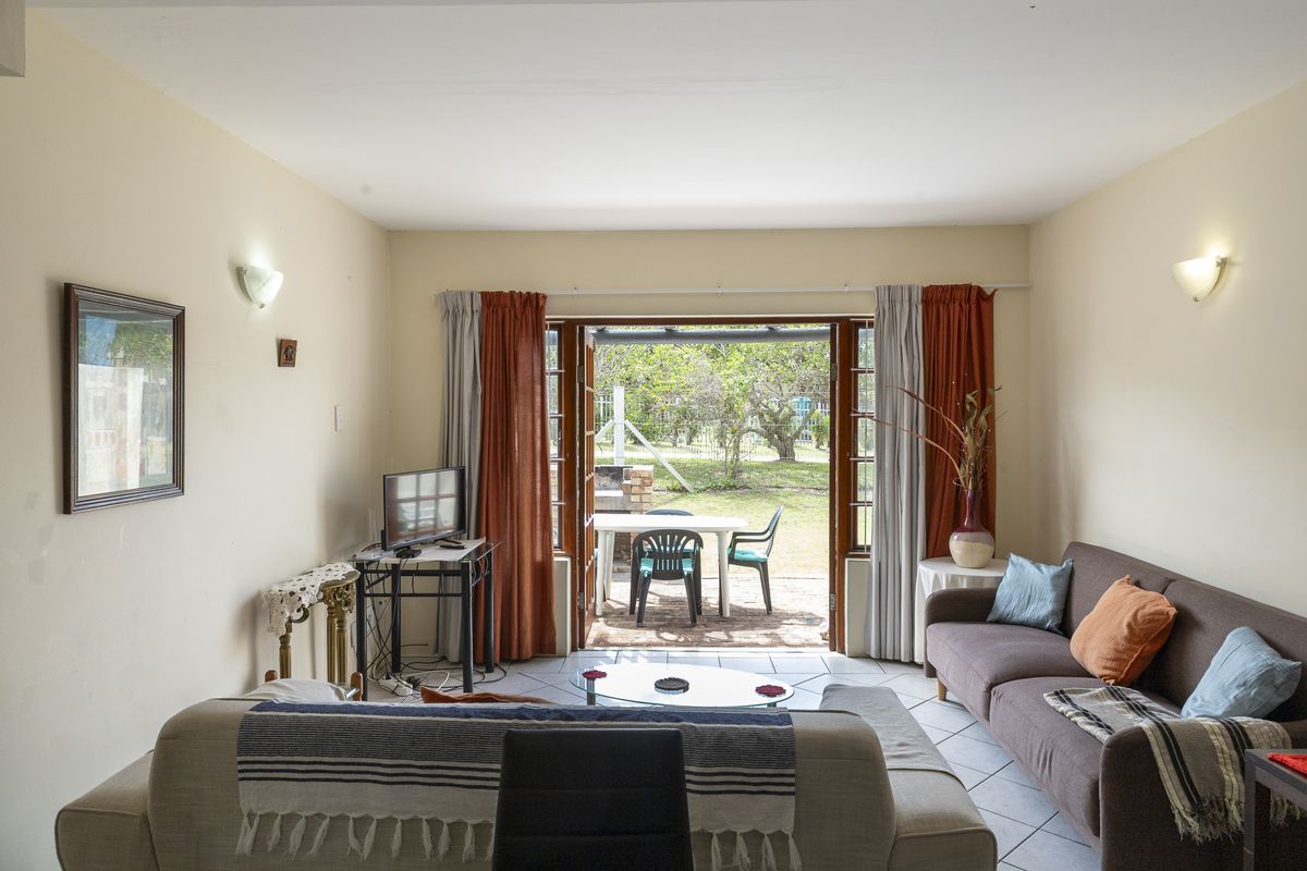 A living room featuring tiled flooring and double glass doors that open onto an outdoor patio area, providing natural light and garden access.