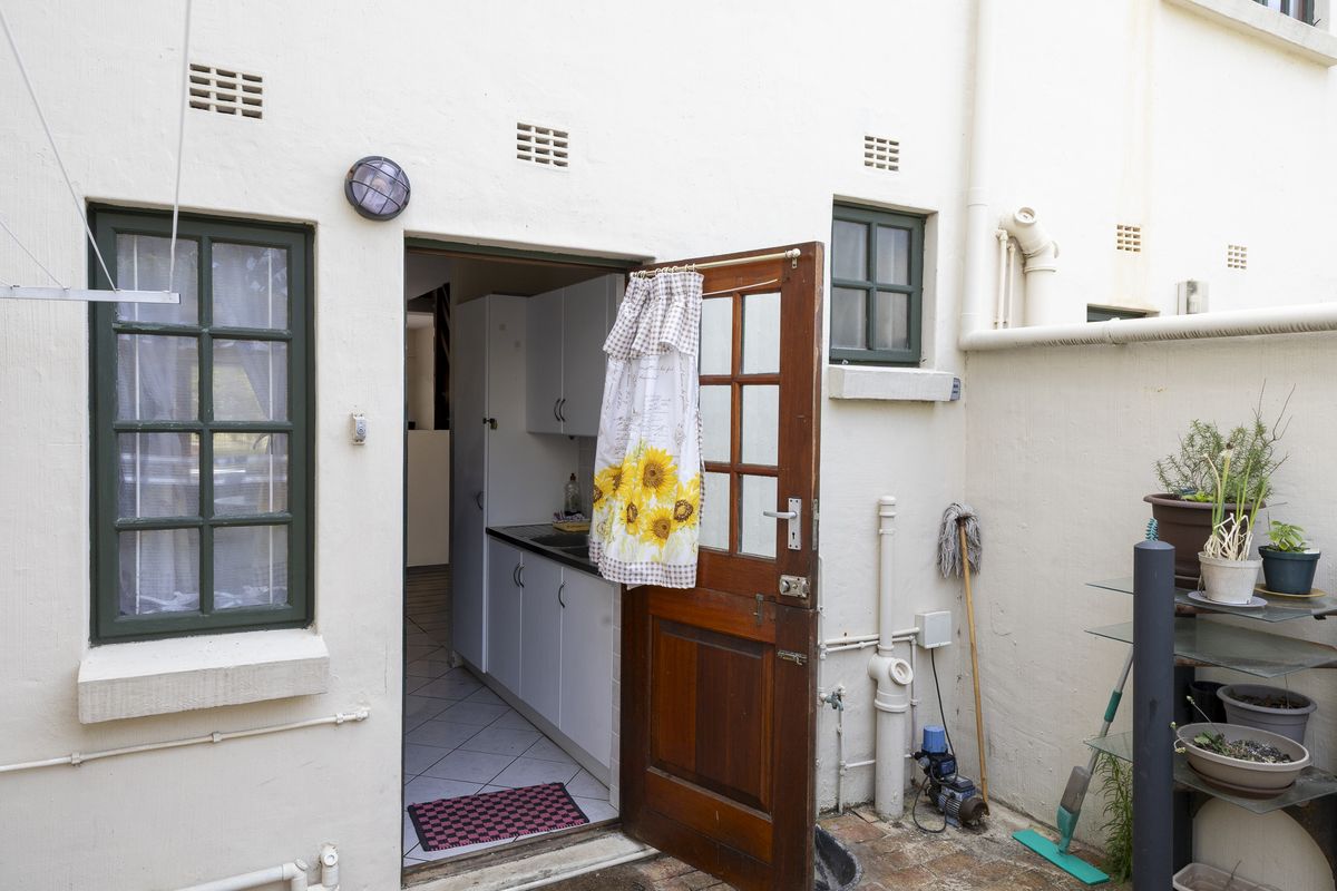 Rear exterior view of the townhouse showing a timber door leading into the kitchen area with external plumbing and ventilation features.