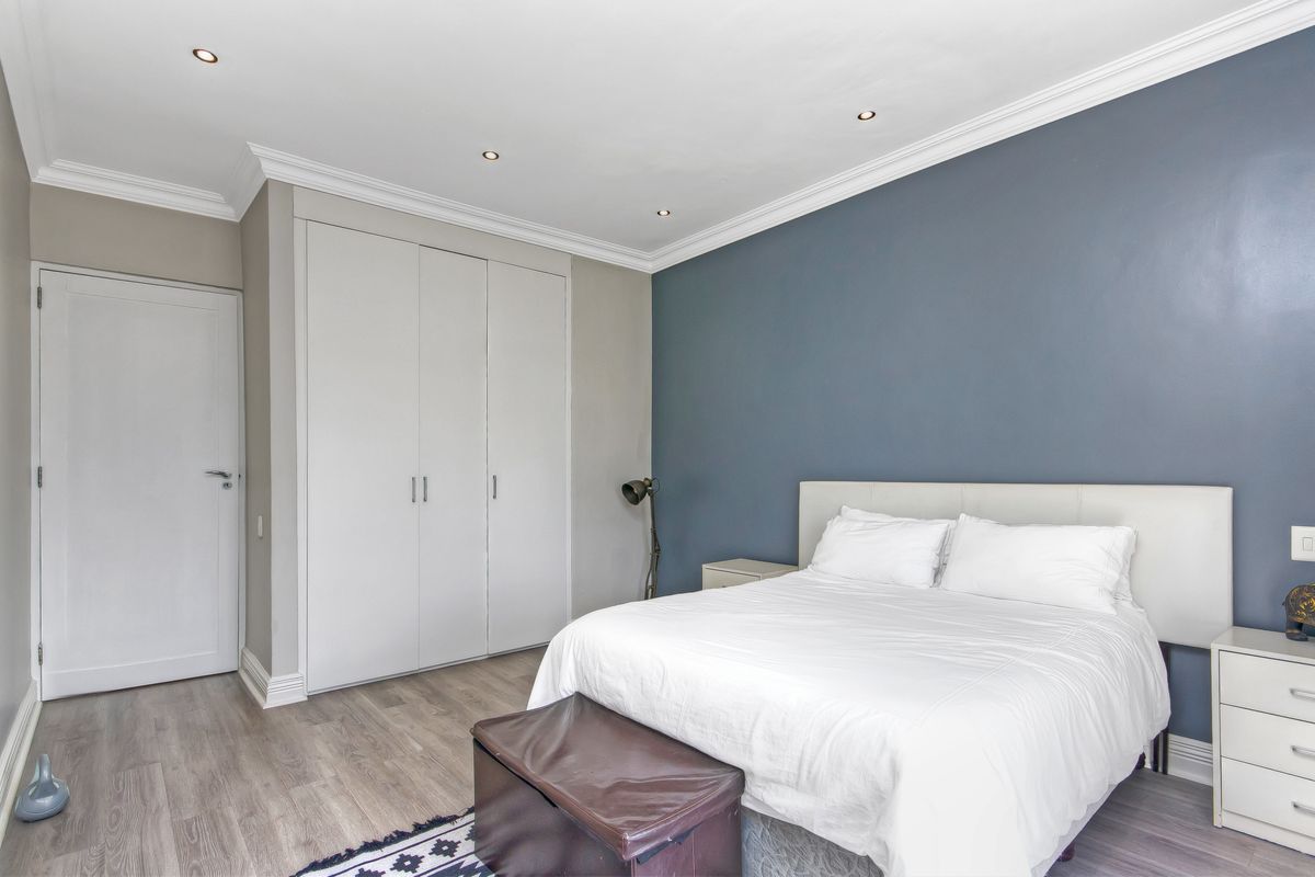 A well-maintained bedroom featuring built-in wardrobes, recessed ceiling lighting, crown molding, and modern wood-look flooring.