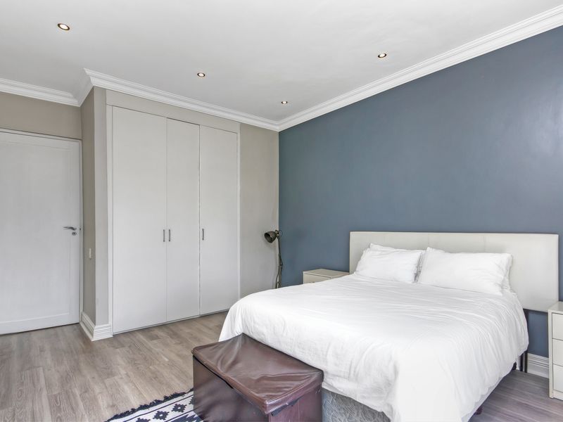 A well-maintained bedroom featuring built-in wardrobes, recessed ceiling lighting, crown molding, and modern wood-look flooring.