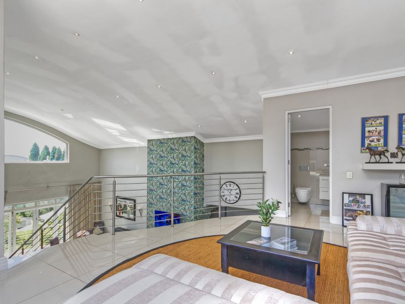 Spacious open-plan living area featuring high vaulted ceilings, tiled flooring, a modern stainless steel balustrade, and direct access to an en-suite bathroom.