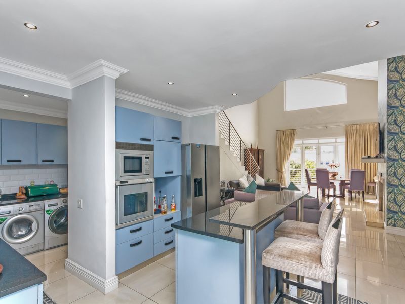 Open-plan kitchen and living area featuring blue cabinetry, built-in oven and microwave, granite countertops, and a breakfast bar, flowing into a spacious lounge.