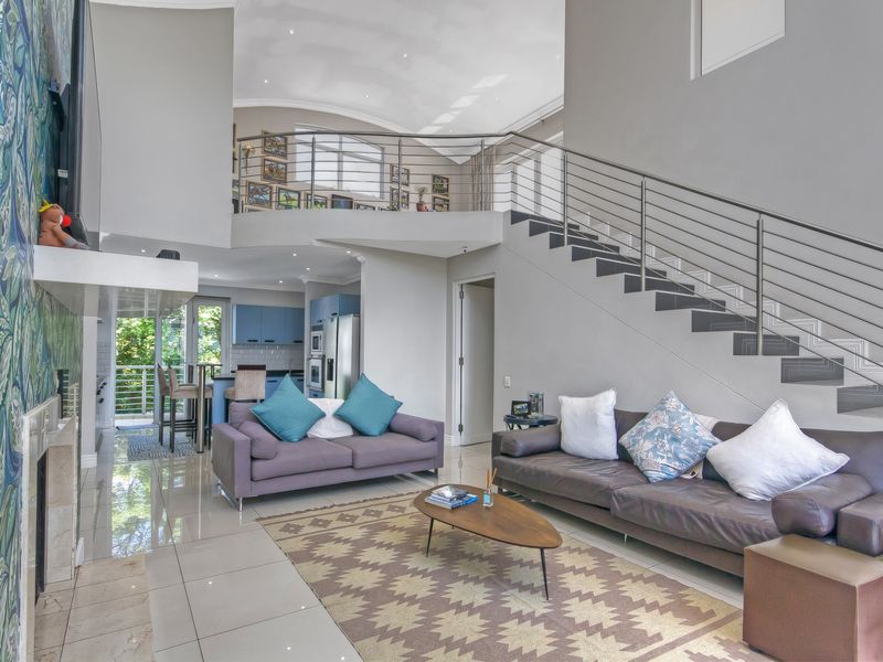 Spacious open-plan living area featuring a double-volume ceiling, a modern staircase with stainless steel railings, and a mezzanine level overlooking the main floor.
