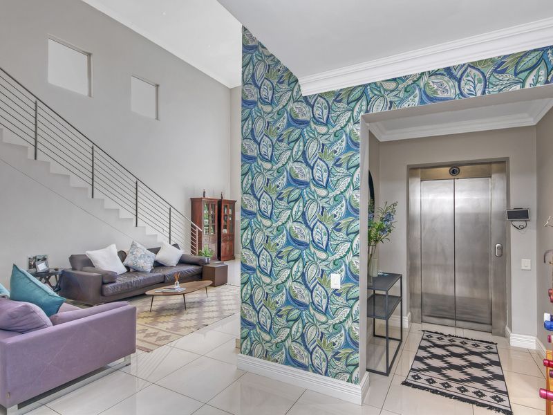 Spacious entrance foyer featuring a private elevator, tiled flooring, and a striking feature wall, leading into an open-plan living area with a staircase.