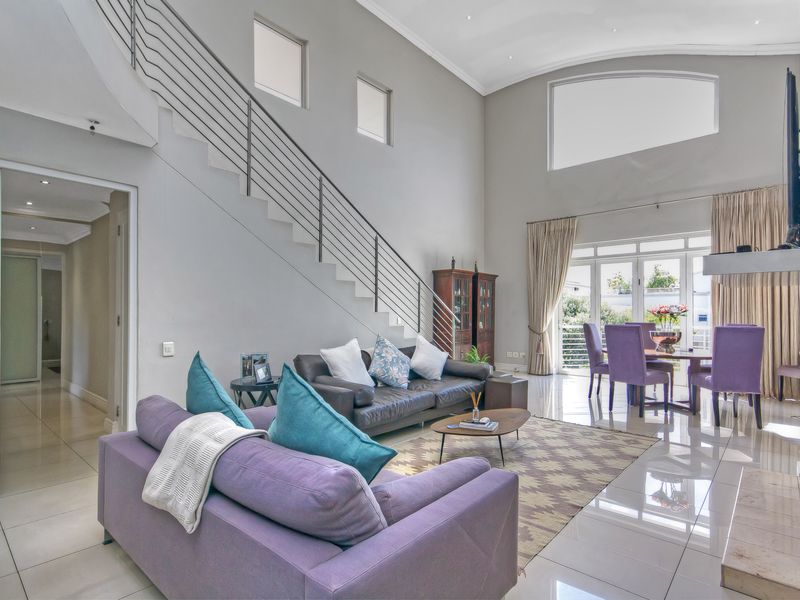 Spacious open-plan living and dining area featuring high vaulted ceilings, polished tile flooring, and a modern staircase with stainless steel balustrades.