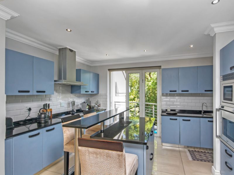 Modern kitchen featuring blue cabinetry, black granite countertops, subway tile backsplash, stainless steel extractor fan, and built-in oven, with direct access to a balcony.