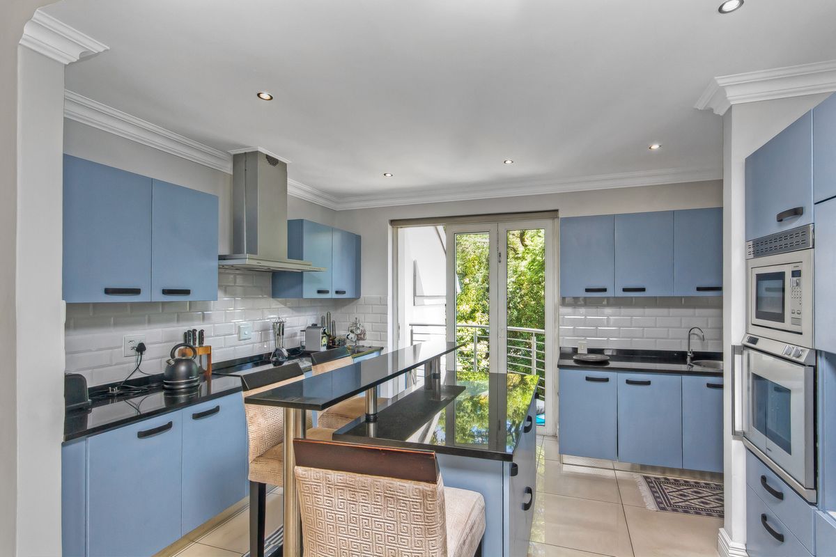 Modern kitchen featuring blue cabinetry, black granite countertops, subway tile backsplash, stainless steel extractor fan, and built-in oven, with direct access to a balcony.