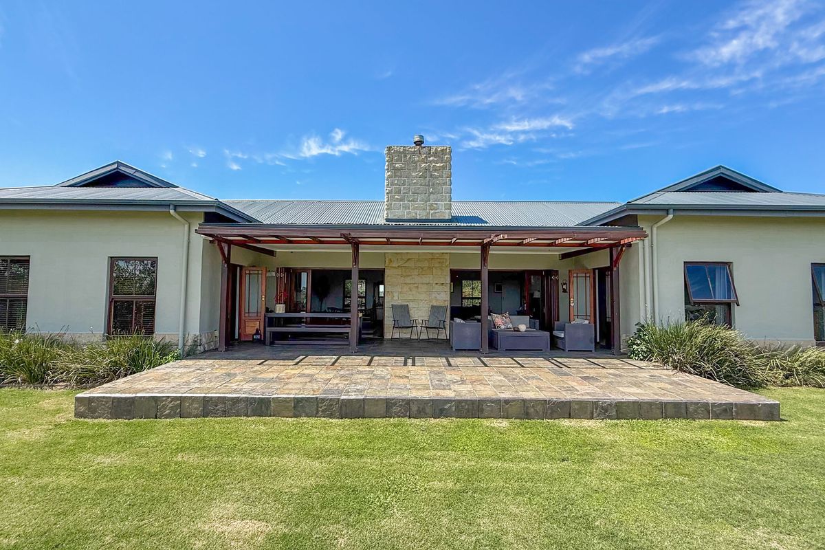 Spacious rear exterior view featuring a covered patio with a stone fireplace, tiled flooring, and a well-maintained lawn.