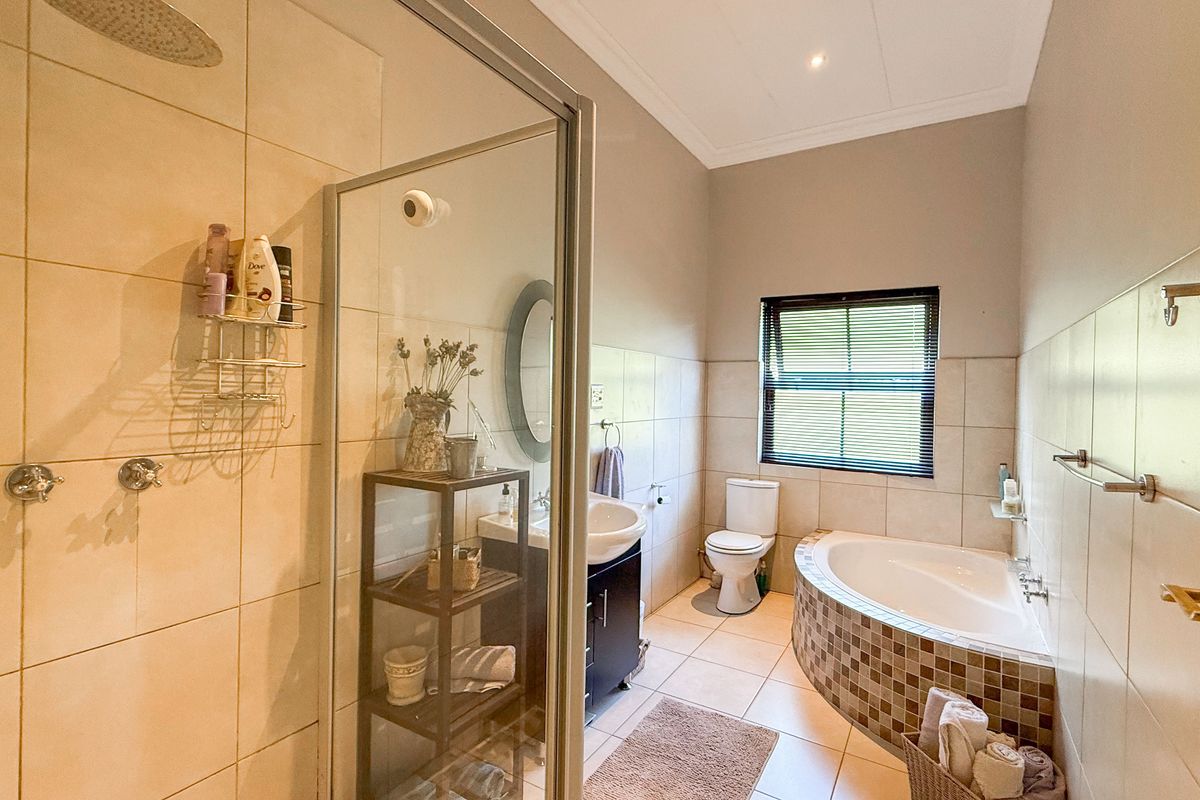 A functional bathroom featuring a glass-enclosed shower, a corner bathtub with mosaic tiling, a vanity basin, and a toilet.