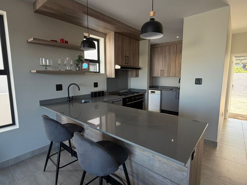 Modern kitchen featuring quartz countertops, built-in cabinetry, gas hob, and a breakfast bar, finished with contemporary pendant lighting and tiled flooring.