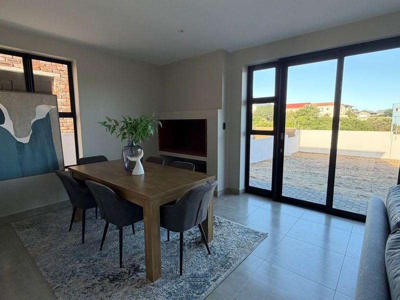 Modern open-plan living and dining area featuring large sliding glass doors, tiled flooring, and a built-in recessed fireplace.
