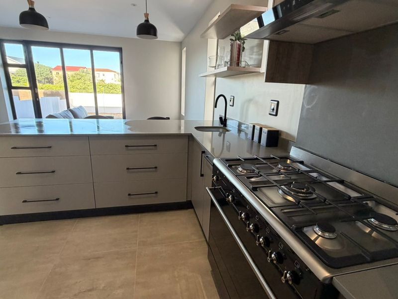 Modern kitchen featuring stone countertops, gas stove, extractor fan, and sleek cabinetry, seamlessly flowing into an open-plan living area with sliding glass doors.