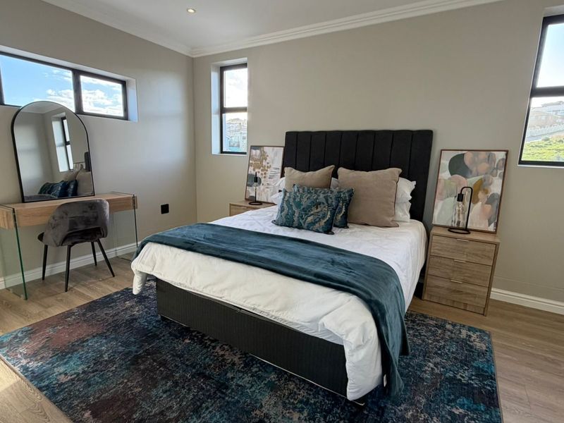 A well-maintained bedroom featuring modern laminate flooring, neutral wall tones, recessed downlighting, and large aluminium-framed windows providing ample natural light.