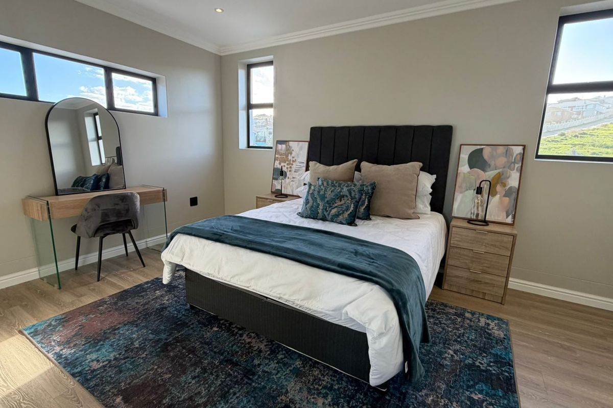 A well-maintained bedroom featuring modern laminate flooring, neutral wall tones, recessed downlighting, and large aluminium-framed windows providing ample natural light.