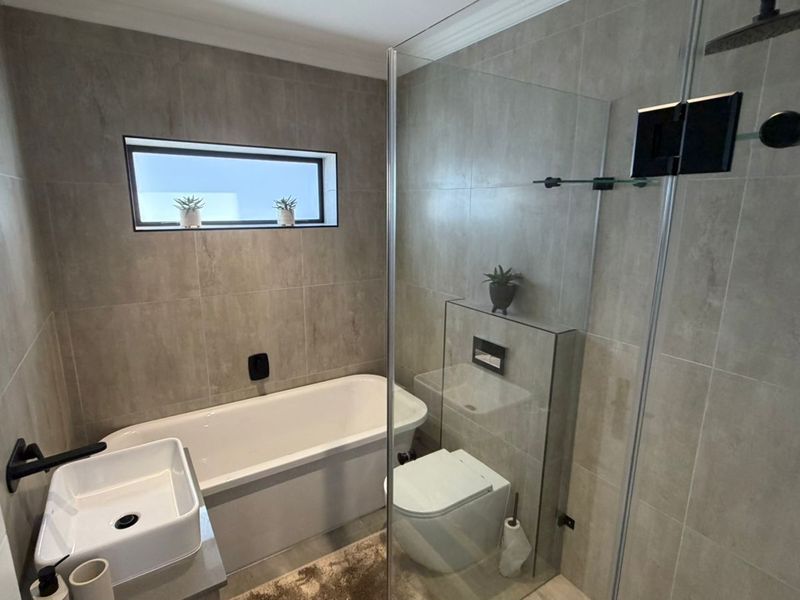 Modern bathroom featuring a sleek freestanding bathtub, walk-in shower with glass screen, wall-hung toilet, and contemporary matte black fixtures throughout.