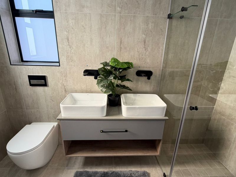 Modern bathroom featuring a double vanity with vessel sinks, wall-mounted toilet, and a glass-enclosed shower with contemporary stone-look tiling.