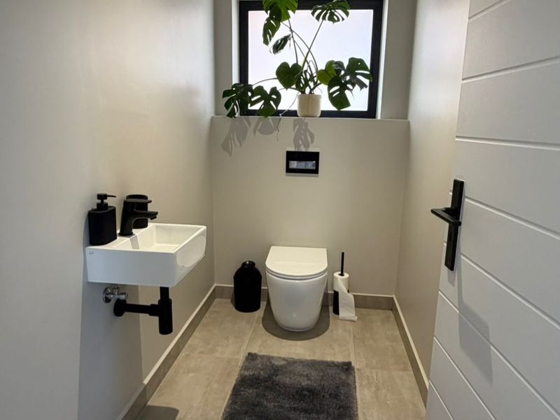 A modern, minimalist guest bathroom featuring a wall-hung toilet, wall-mounted basin with black fixtures, and neutral floor tiling.