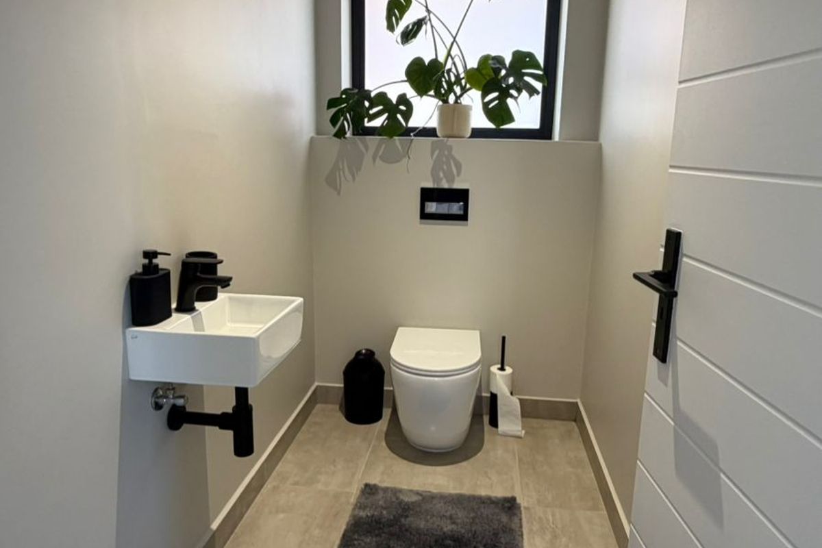 A modern, minimalist guest bathroom featuring a wall-hung toilet, wall-mounted basin with black fixtures, and neutral floor tiling.