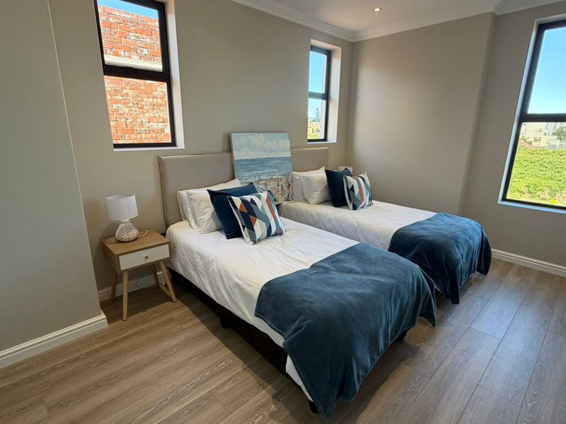 A well-maintained bedroom featuring modern laminate flooring, neutral wall tones, and large aluminium-framed windows providing ample natural light.