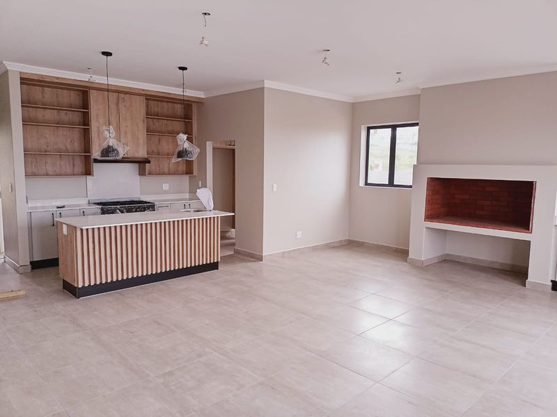 Spacious open-plan living area featuring a modern kitchen with island, built-in fireplace, and neutral tiled flooring, currently in a near-complete state.