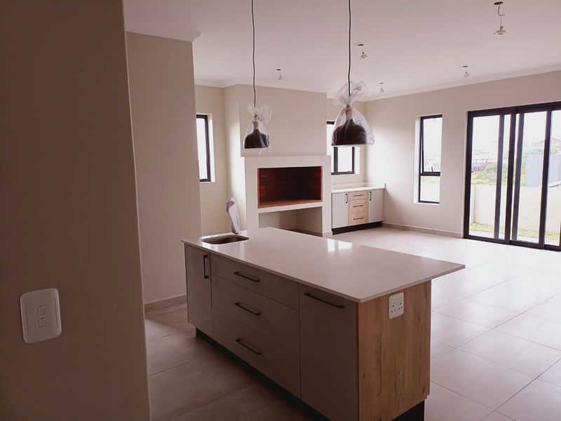 Spacious open-plan living area featuring a modern kitchen island, built-in fireplace, tiled flooring, and large sliding doors leading to the exterior.