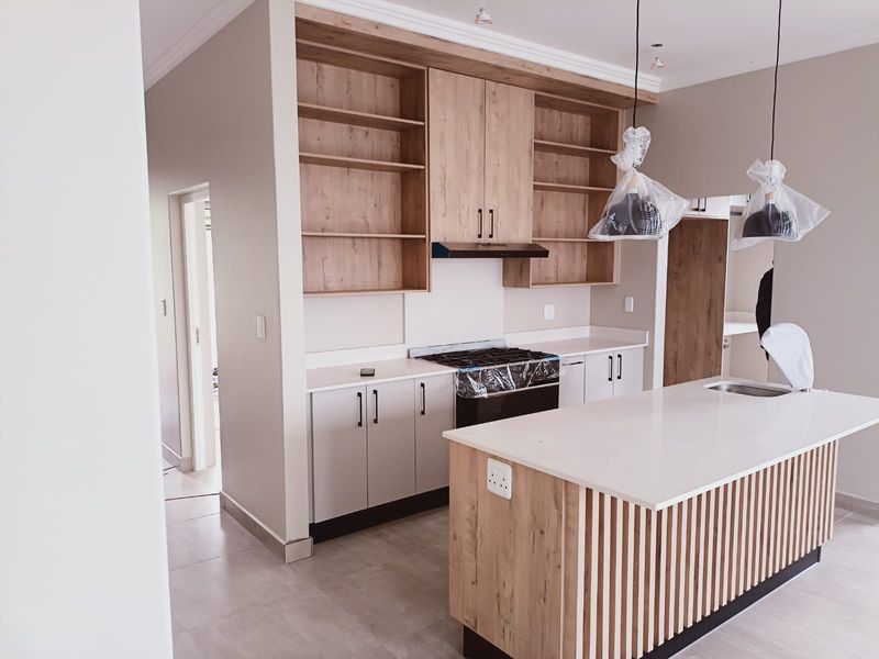 Modern kitchen featuring light wood cabinetry, stone countertops, a central island with slatted detailing, and integrated gas hob and extractor fan.