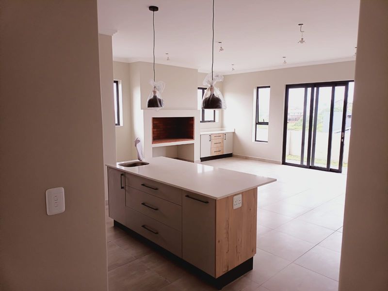 Modern open-plan living area featuring a sleek kitchen island with stone countertops, built-in fireplace, and large sliding doors leading to the exterior.