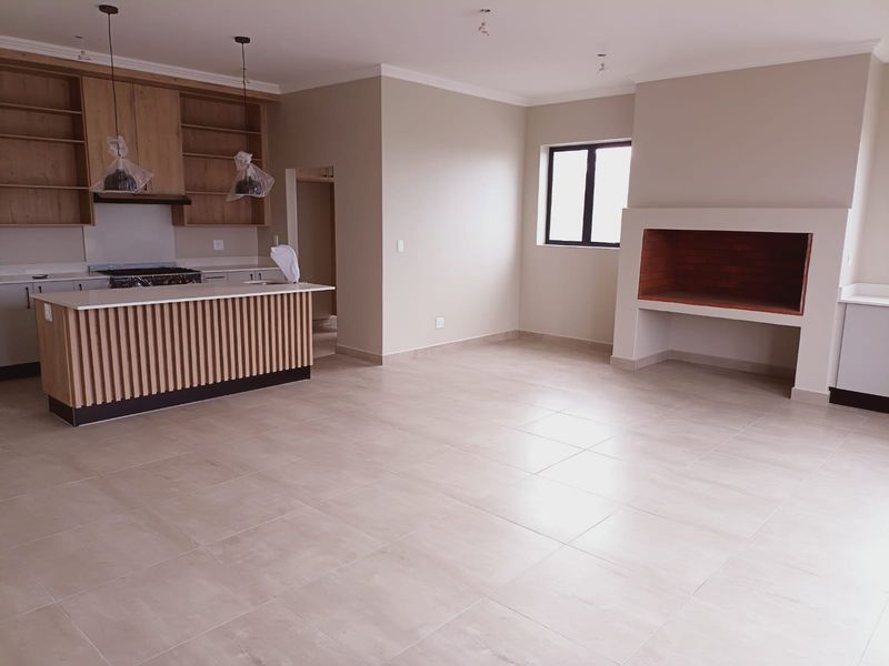 Spacious open-plan living area featuring a modern kitchen with island, built-in cabinetry, and a prominent brick fireplace, finished with neutral floor tiles.
