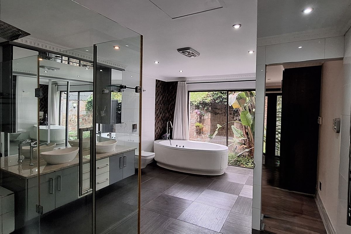 Modern, spacious bathroom featuring a freestanding bathtub, double vanity, glass-enclosed rain shower, and heated towel rail with large windows overlooking the garden.
