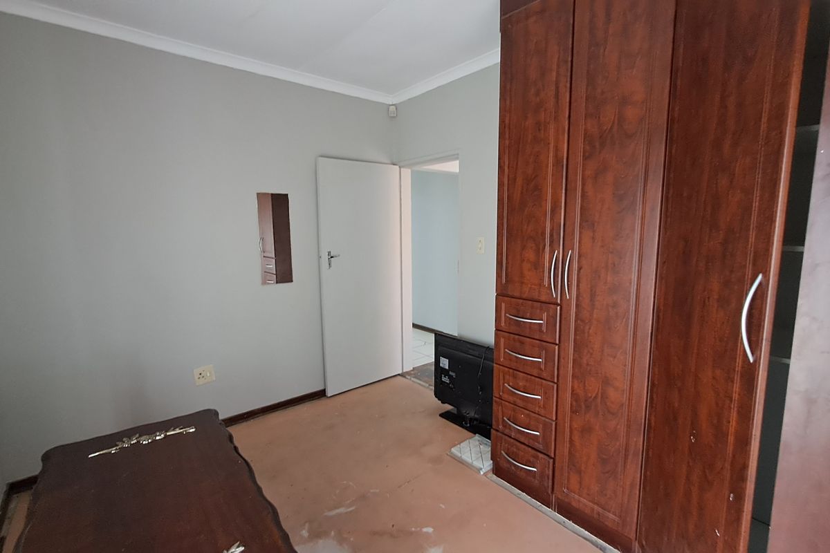 A bedroom featuring built-in wooden cupboards, neutral wall paint, and coving. The room requires flooring updates and general cosmetic refurbishment.