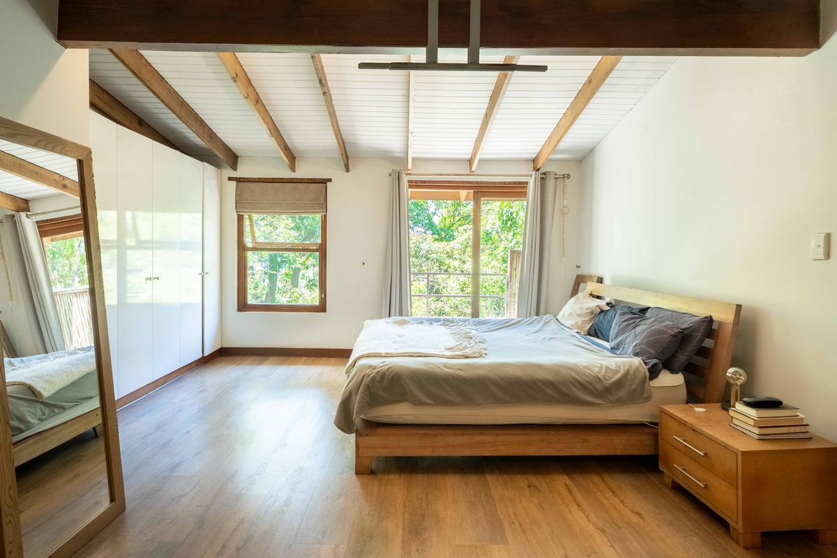 Spacious bedroom featuring exposed timber ceiling beams, built-in wardrobes, and timber flooring, with large windows providing natural light and garden views.
