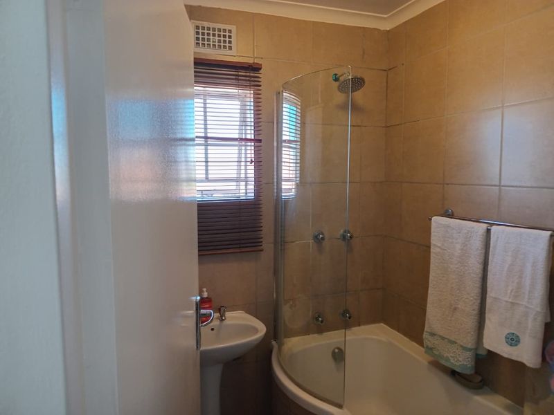 A functional bathroom featuring a pedestal basin, a bathtub with a curved glass shower screen, and neutral wall tiling.