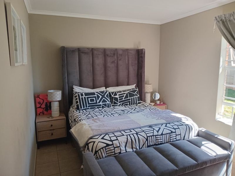 A well-lit bedroom featuring neutral wall tones, tiled flooring, and a large window allowing natural light.