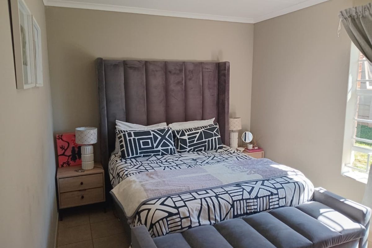 A well-lit bedroom featuring neutral wall tones, tiled flooring, and a large window allowing natural light.