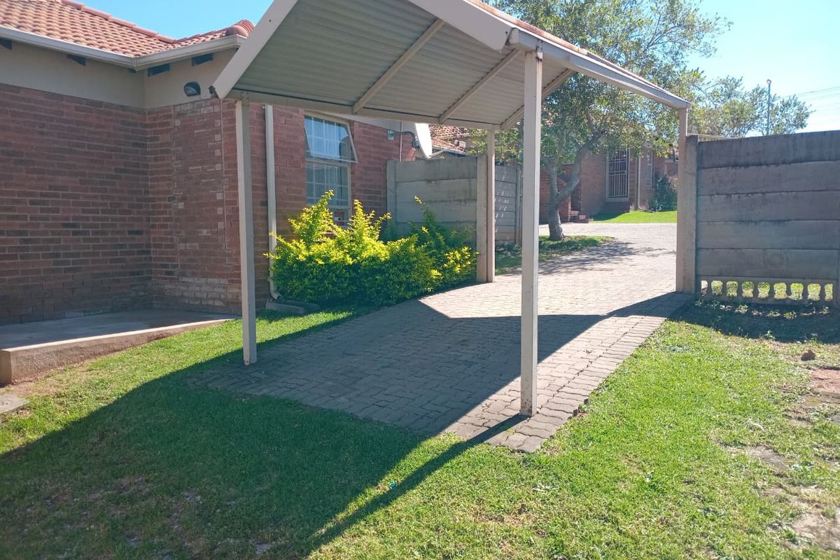 A rear exterior view of the townhouse featuring a covered carport, brick paving, and a precast concrete boundary wall.