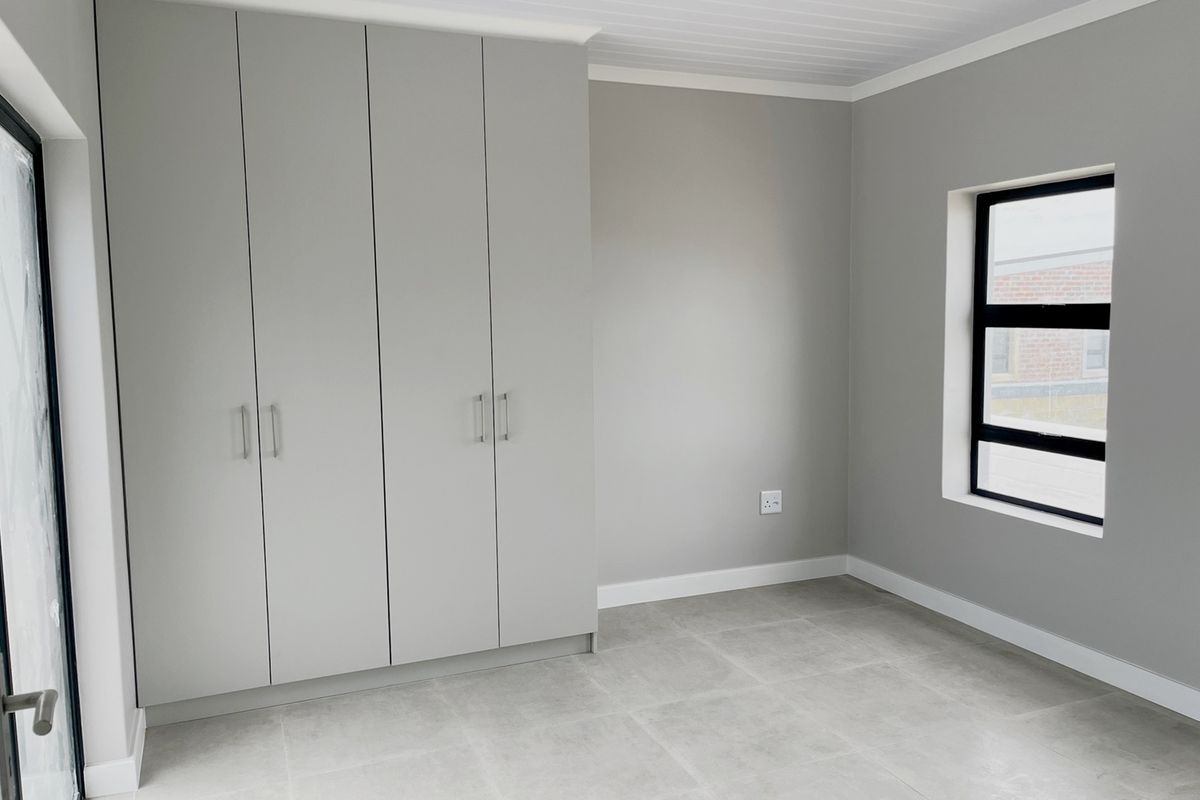 A bright, modern bedroom featuring neutral grey walls, tiled flooring, and built-in floor-to-ceiling cabinetry.