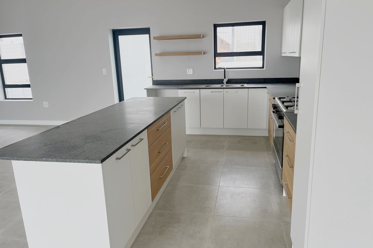 Modern kitchen featuring a central island, stone countertops, built-in oven and hob, and sleek two-tone cabinetry with ample storage space.