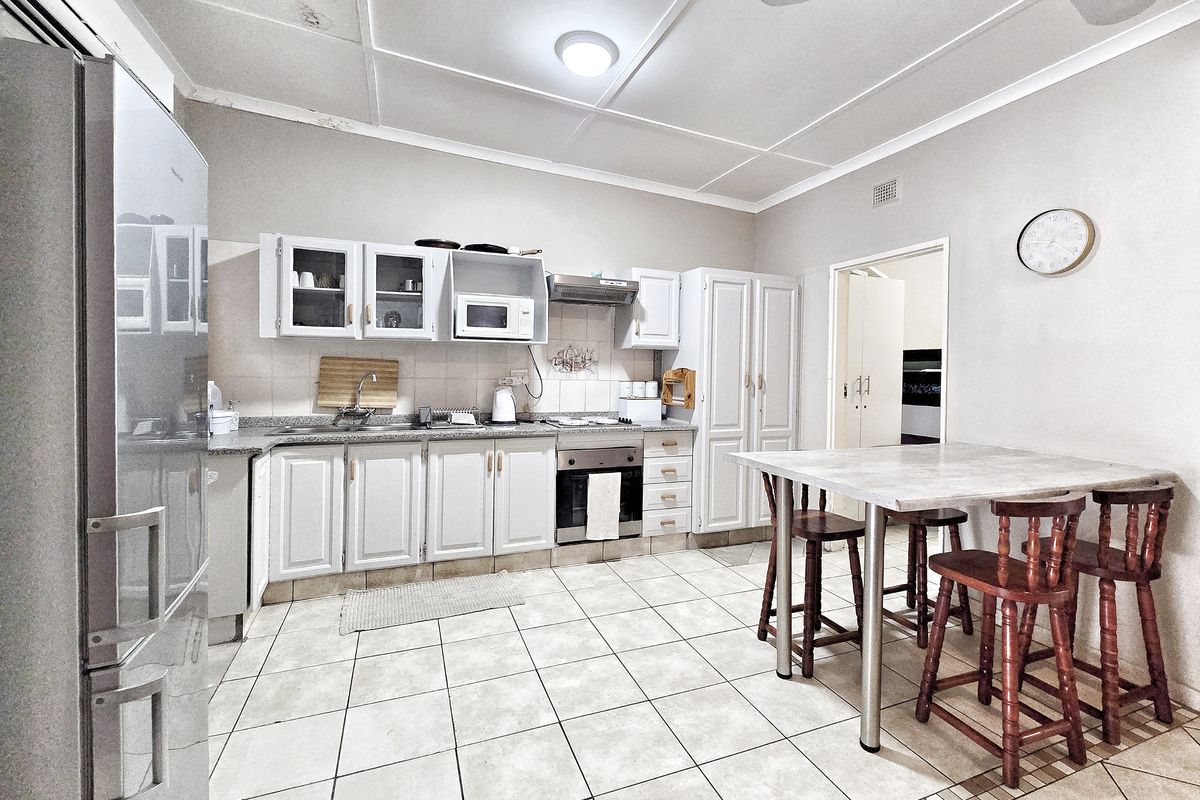 Functional kitchen featuring built-in cabinetry, granite countertops, integrated oven, and extractor fan, with tiled flooring and direct access to adjacent living areas.