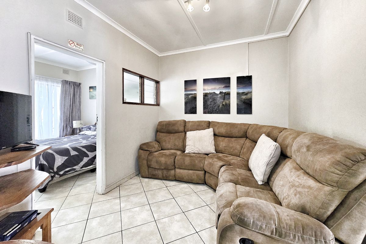 A living room area featuring ceramic floor tiles and a coved ceiling, with an open doorway leading into an adjacent bedroom.