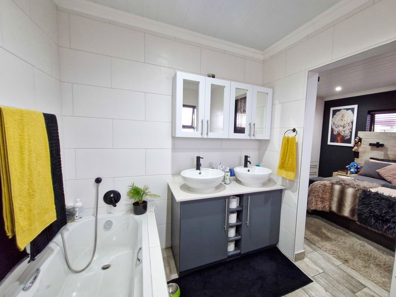 Modern bathroom featuring a double vanity with vessel sinks, built-in medicine cabinet, and a tiled bathtub area, adjacent to a bedroom.