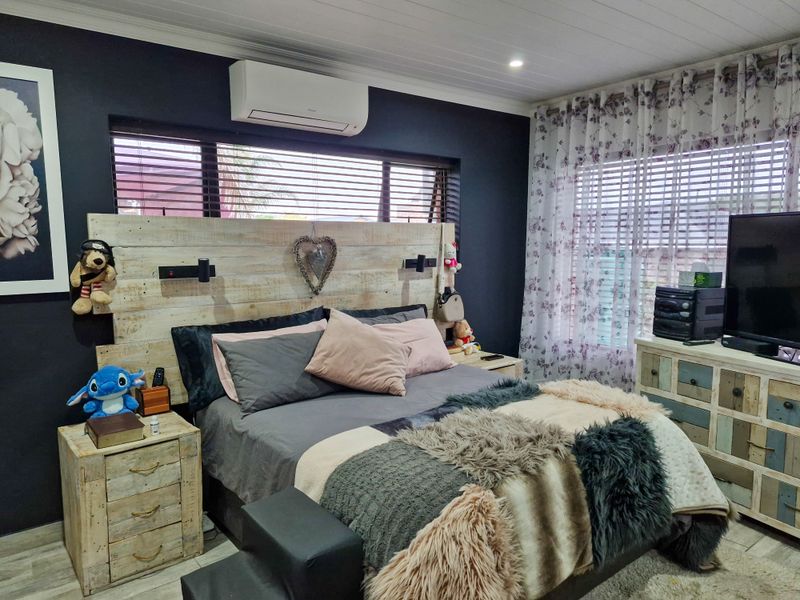 A well-maintained bedroom featuring dark accent walls, a split-system air conditioner, and timber-look tile flooring with large windows and venetian blinds.