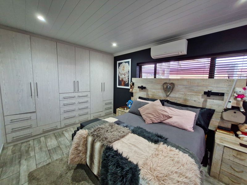 A well-maintained bedroom featuring extensive built-in cabinetry, timber-look flooring, a split-system air conditioner, and a modern tongue and groove ceiling finish.
