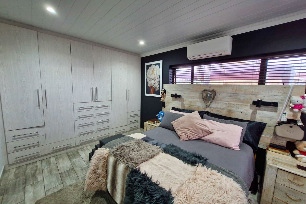 A well-maintained bedroom featuring extensive built-in cabinetry, timber-look flooring, a split-system air conditioner, and a modern tongue and groove ceiling finish.