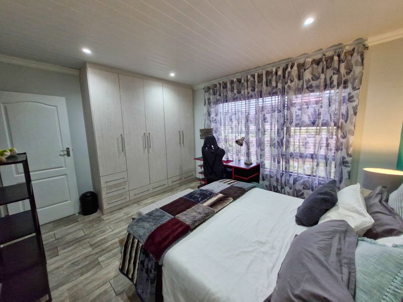 A well-maintained bedroom featuring built-in cupboards, tiled flooring, and a modern panelled ceiling with recessed lighting.