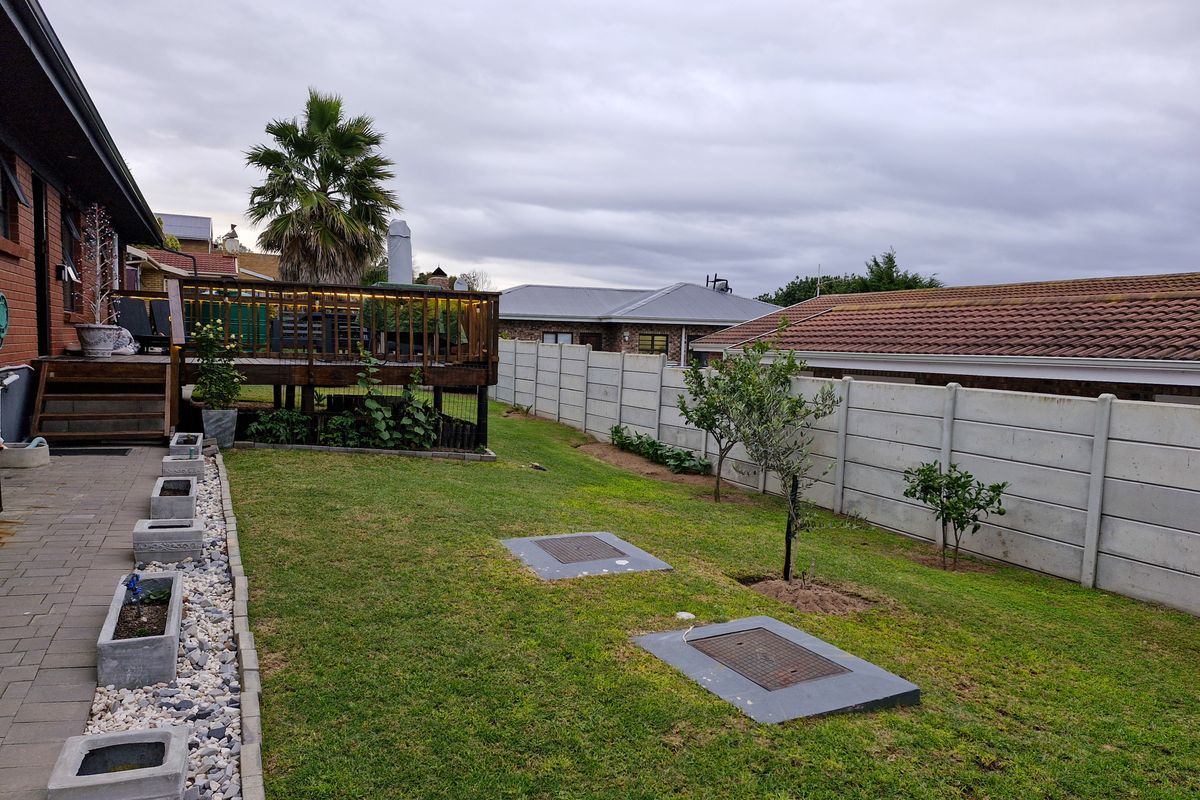 A well-maintained rear garden featuring a raised timber deck, paved patio area, and a secure precast concrete boundary wall.