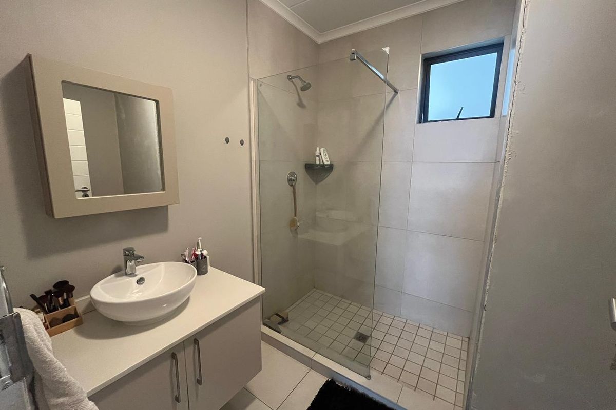 Modern bathroom featuring a vessel sink vanity, walk-in shower with glass screen, and neutral wall tiling.