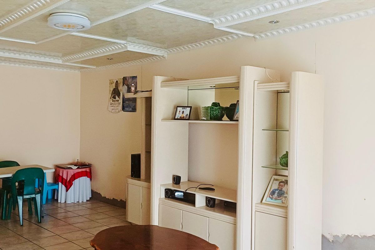Living room featuring tiled flooring, a decorative coffered ceiling, and built-in display cabinetry, showing signs of wear on the lower wall surfaces.